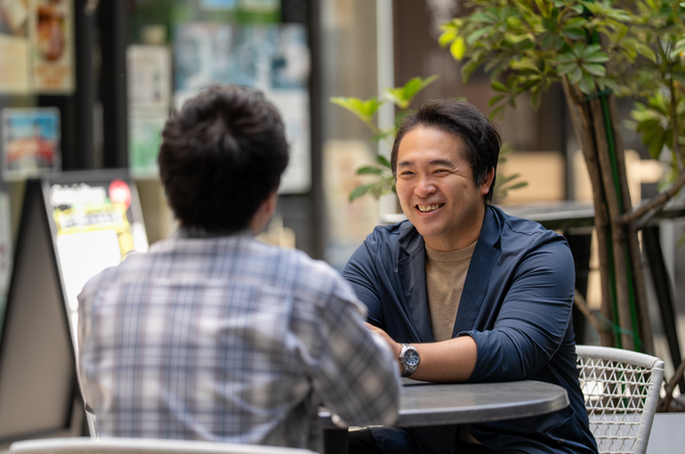  カフェで向き合い笑顔で会話する男性。婚活や相談の場で、相手を引き込む良好なコミュニケーションと親しみやすい雰囲気を表現している。