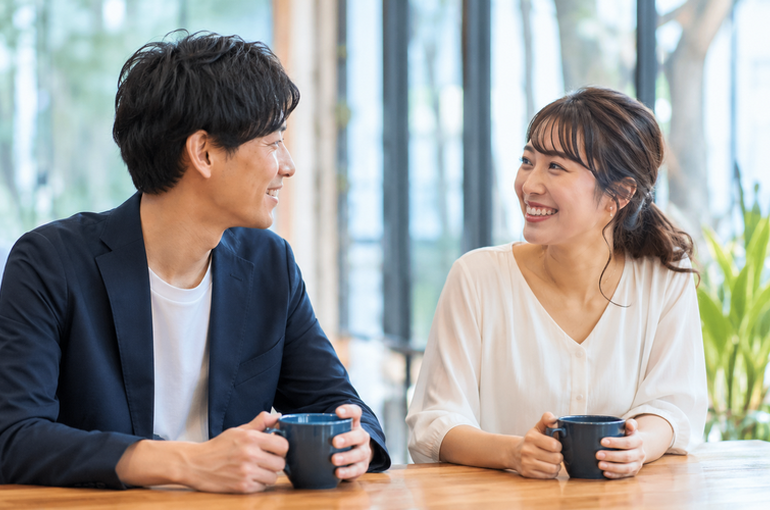  カフェで向かい合ってコーヒーを飲みながら笑顔で会話する男女のカップル。リラックスした雰囲気でコミュニケーションを取る様子から楽転力の重要性が伝わる婚活デートのイメージ。