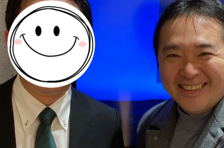 スーツ姿の中年男性2人が室内で記念撮影をしており、右側の男性が満面の笑顔を見せ、左側の男性は顔にスマイルマークが描かれた状態で、婚活やお見合い成功の喜びを表現している画像